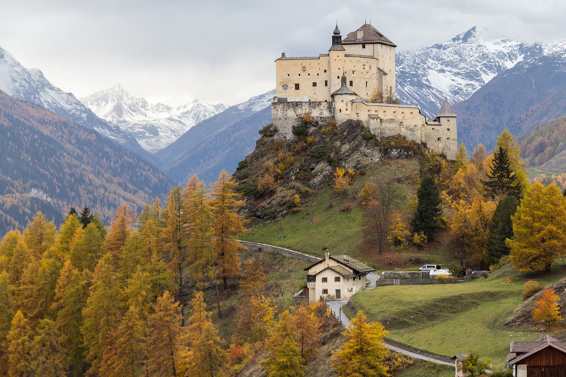 Tarasp Castle above golden larches, with snow on the peaks behind it